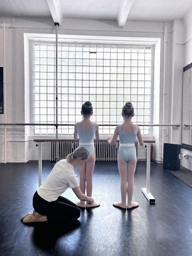 Anastasia correcting two young students' foot placement in a mini-group class